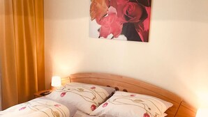 A double bed with floral bedding, a wooden headboard, a nightstand with a lamp, and a painting of flowers on the wall. - Brauneggerhof Gasthof Mayer (Raxendorf)