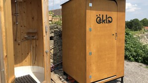 Una sauna portátil de madera con ducha, un banco y una puerta que muestra el logotipo "öklö".