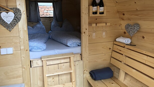 Acogedora habitación de cabaña de madera con cama, dos botellas de vino, adornos con forma de corazón y una ventana con cortinas de cuadros.