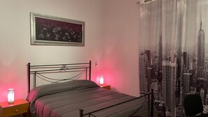 A bedroom with a bed, a nightstand, a lamp, a framed picture, and a curtain with a cityscape design. - STATION'S ROOM (AVELLINO)