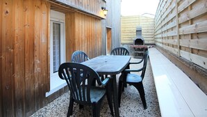 Un patio exterior de madera con una mesa, sillas, una parrilla de barbacoa y una valla de madera.