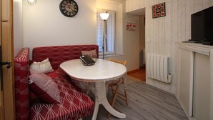 Una habitación acogedora con un sofá rojo estampado, una mesita redonda con una cesta, un reloj de pared y un televisor sobre un mueble.
