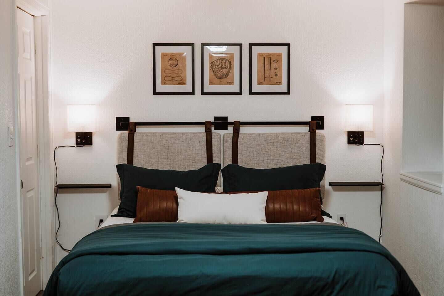 A bedroom with a bed, headboard, bedside lamps, and three framed pictures on the wall.