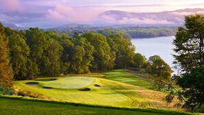 A golf course with bunkers and a water body in the background. - Luxury Loch Lomond Lodge (Alexandria)