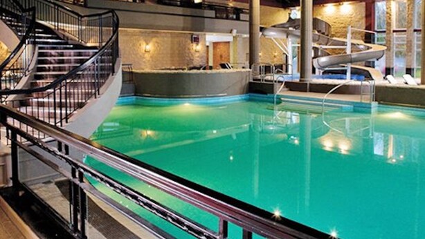 An indoor swimming pool with a central slide, a staircase, and a seating area with a view of the pool. - Luxury Loch Lomond Lodge (Alexandria)