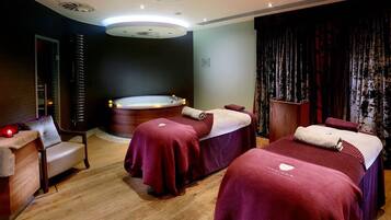 A spa room with two massage beds, a massage chair, a large bathtub, and a wooden reception desk.
