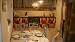 Een eetgedeelte met een ronde tafel voor vier personen, stoelen, een keuken op de achtergrond en een houten plafond.