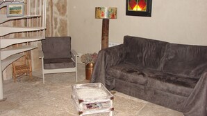 Een woonkamer met een bruine bank, een grijze fauteuil, een klein houten tafeltje en een trap met een witte leuning.