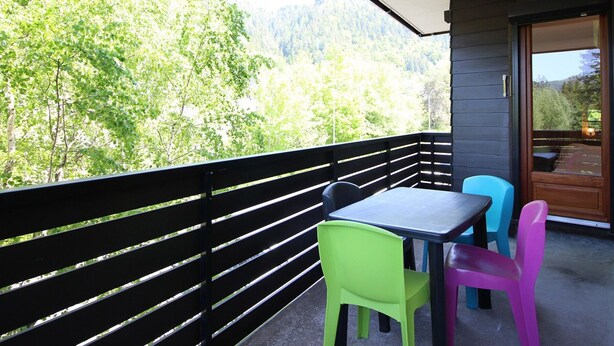 Un balcon avec une table et des chaises, donnant sur une zone boisée.