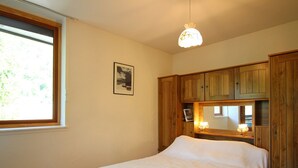 Une chambre à coucher avec un lit, une armoire en bois, une fenêtre et un luminaire suspendu.