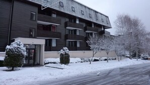 Un bâtiment moderne doté de nombreux balcons, d’une entrée sécurisée et entouré d’un paysage enneigé.