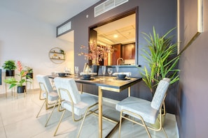 A dining area with a table set for four, surrounded by chairs with a light fabric upholstery and gold legs.