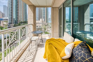 A balcony with a sofa, a table, and chairs, overlooking a cityscape with high-rise buildings.