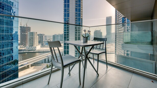 Un balcon moderne avec une balustrade en verre, deux chaises et une table agrémentée d’une plante en pot.