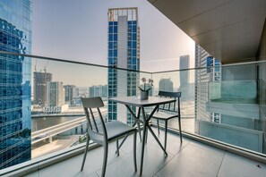 Un balcon moderne avec une balustrade en verre, deux chaises et une table agrémentée d’une plante en pot.