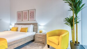 Une chambre moderne avec un lit, une table de chevet, une lampe et un fauteuil jaune. Trois œuvres d’art encadrées sont accrochées au mur au-dessus du lit.