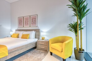 Un dormitori modern amb llit, taula de nit, làmpada i un butac armchair groc. Hi ha tres quadres amb marc a la paret sobre el llit.