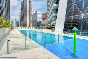 Una piscina al terrat amb aigua blava cristal·lina, envoltada d'edificis alts i un disseny arquitectònic modern.