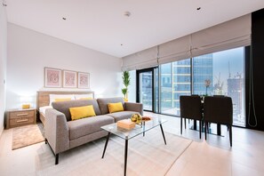A modern living room with a sofa, a glass coffee table, a dining area with chairs, and a large window with a city view.