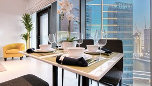 Un espace repas moderne avec une table dressée pour quatre personnes, de grandes fenêtres donnant sur la ville et un fauteuil jaune en arrière-plan.