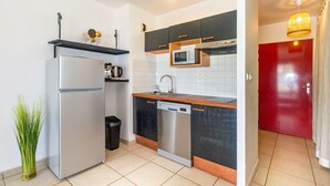 Una cocina moderna con refrigerador, microondas y lavavajillas, y una puerta roja al fondo.