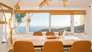 Un comedor con una mesa grande, sillas naranjas y vista al mar.