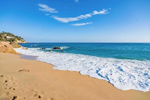 Ein Strand mit klarem blauen Wasser, sandigem Ufer und Felsenformationen.