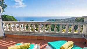 Un balcon avec vue sur la mer, deux chaises longues avec des serviettes et une balustrade blanche.