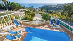 Una piscina con sillones de descanso y vista al mar.