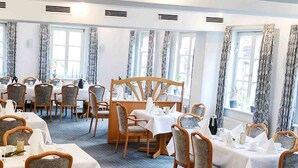 Une salle à manger avec plusieurs tables dressées, ornées de nappes blanches et de chaises en bois.