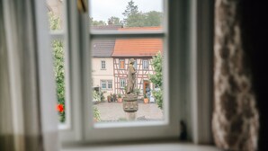 Une vue à travers une fenêtre, avec une statue au premier plan et un bâtiment traditionnel avec un toit rouge en arrière-plan.