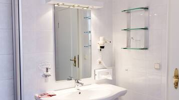 A bathroom with a white sink, a mirror, and a glass shelf unit.
