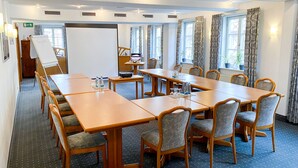 Une salle de conférence équipée d’une longue table, de chaises, d’un tableau blanc et d’un projecteur.