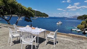Ein Tisch mit Stühlen auf einer Betonfläche mit Blick auf ein Gewässer und Boote.