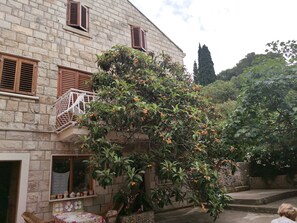 Ein Steinhaus mit Balkon, ein Baum mit orangefarbenen Früchten und Blick auf die umliegende Grünfläche.