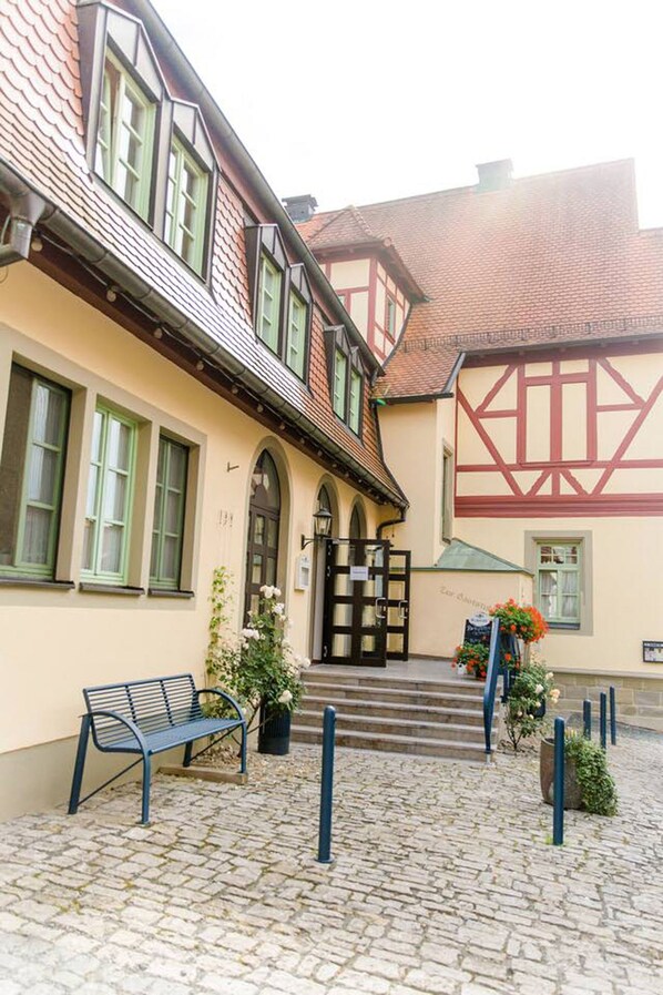 A traditional half-timbered building with a cobblestone courtyard, a bench, and a flower arrangement.