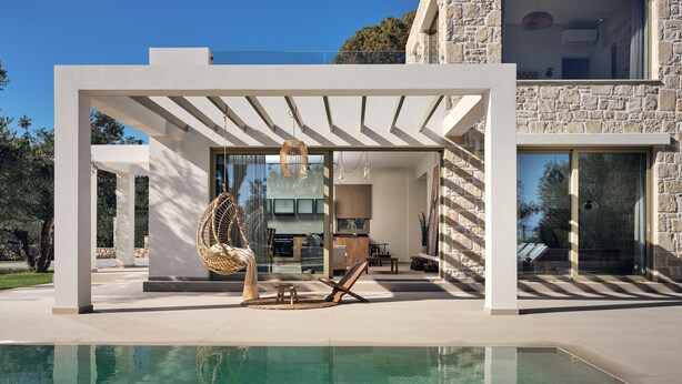A modern house with a pool, a hanging chair, and a stone wall.