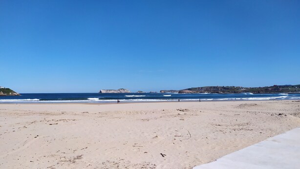 A wide sandy beach with gentle waves and a clear blue sky. - Piso a pie de Playa (Suances)