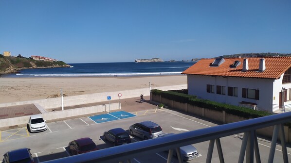 A beach view with a parking area, a building with a red roof, and a clear blue sky.