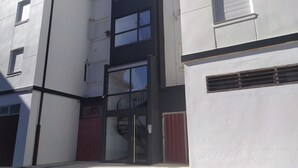 A modern building with a glass entrance, a staircase, and a red door. - Piso a pie de Playa (Suances)