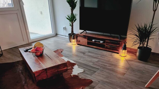 Una sala moderna con una mesa de centro de madera, un televisor de pantalla plana y dos plantas en macetas.