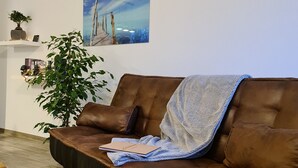 Una sala de estar con un sofá de cuero marrón, una mesa de centro de madera, una planta en maceta y un cuadro en la pared.