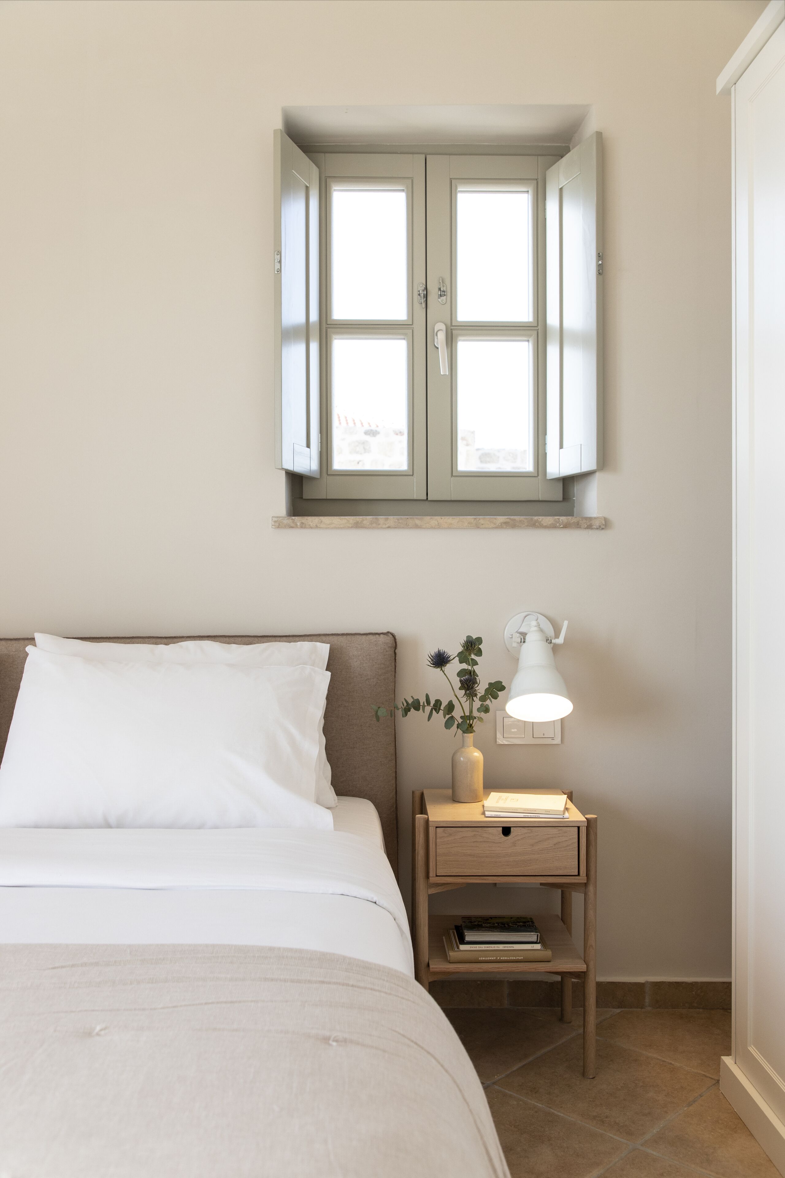 A bedroom with a bed, a nightstand with a lamp, a window with a view, and a door.