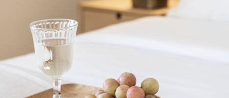 A wooden tray with a glass and a bowl of fruit on a bed.