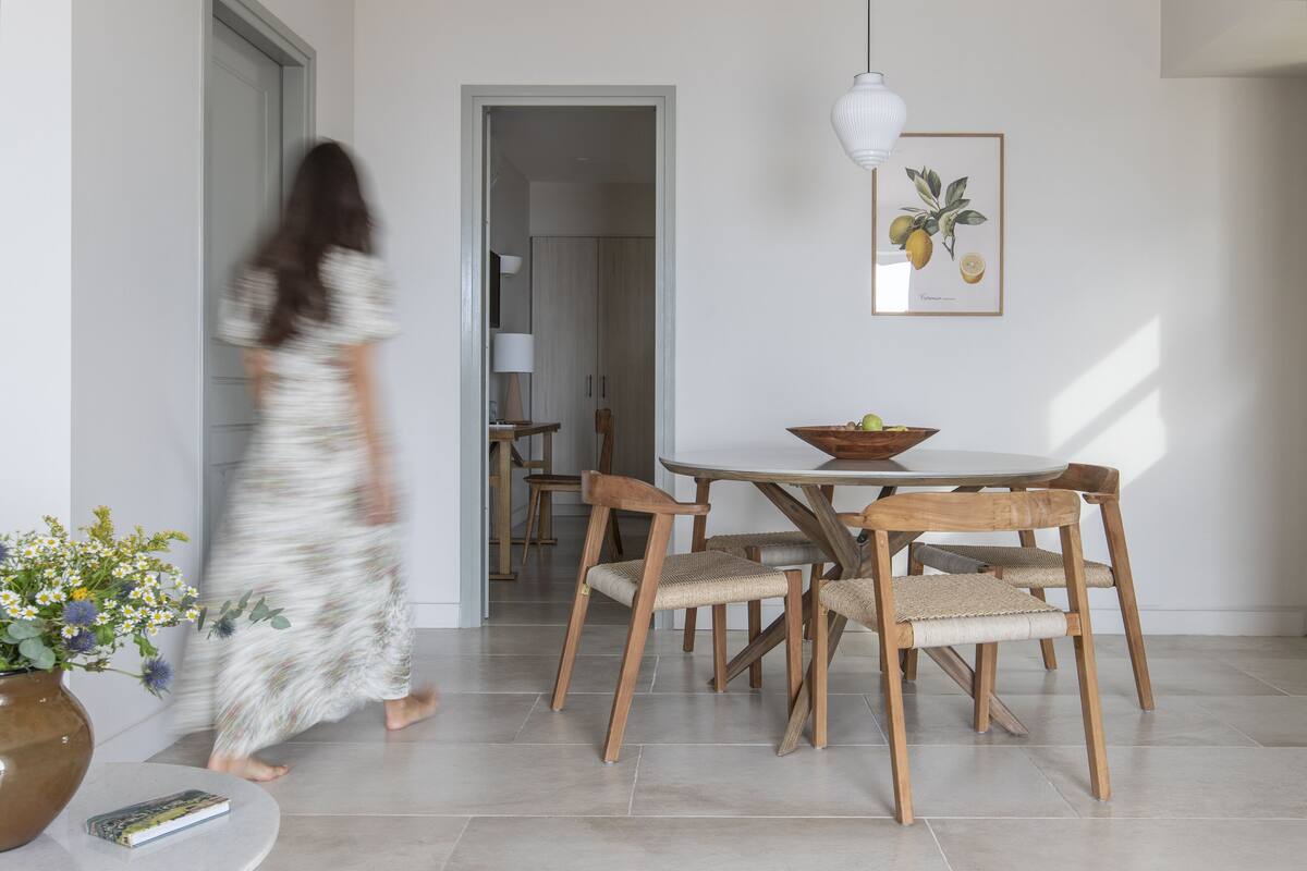 A dining area with a round table, wooden chairs, and a vase with flowers.