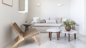 A modern living room with a sofa, a wicker chair, two coffee tables, and a vase with flowers. - Amani Earthy Living (West Mani)