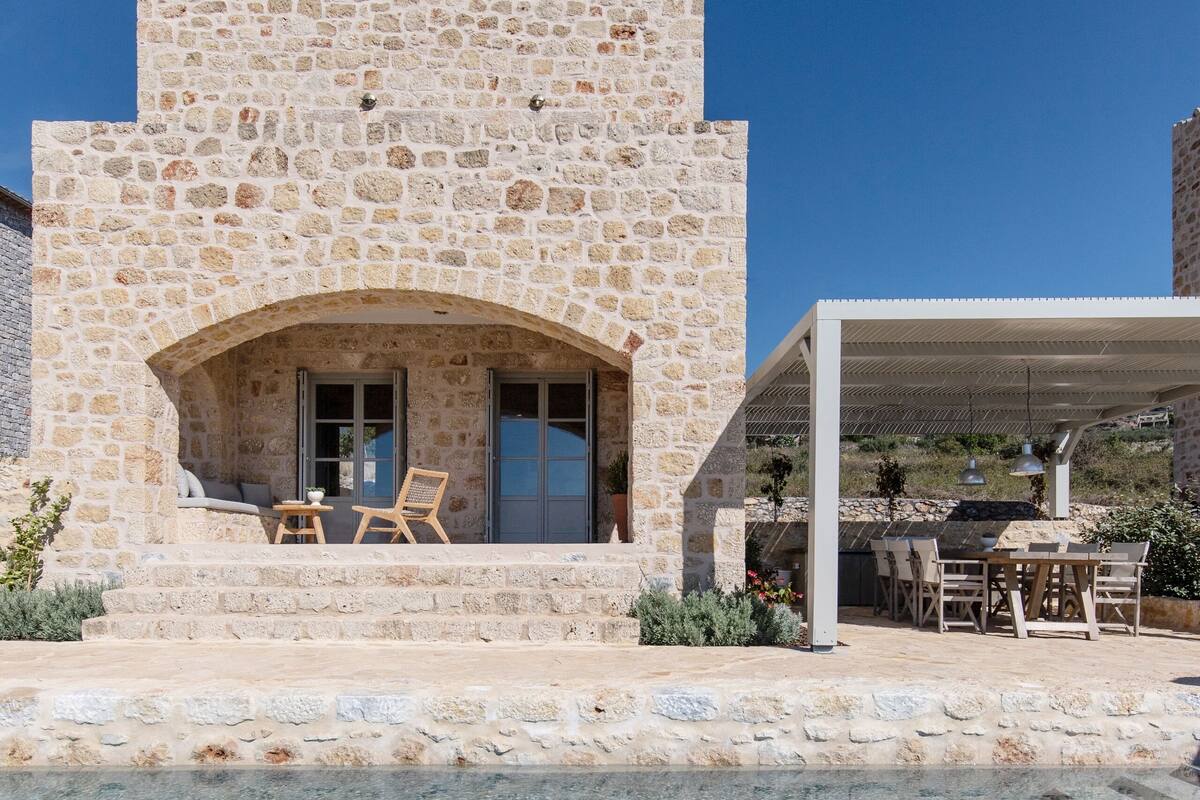 A stone building with a pool, outdoor seating, and a covered patio.
