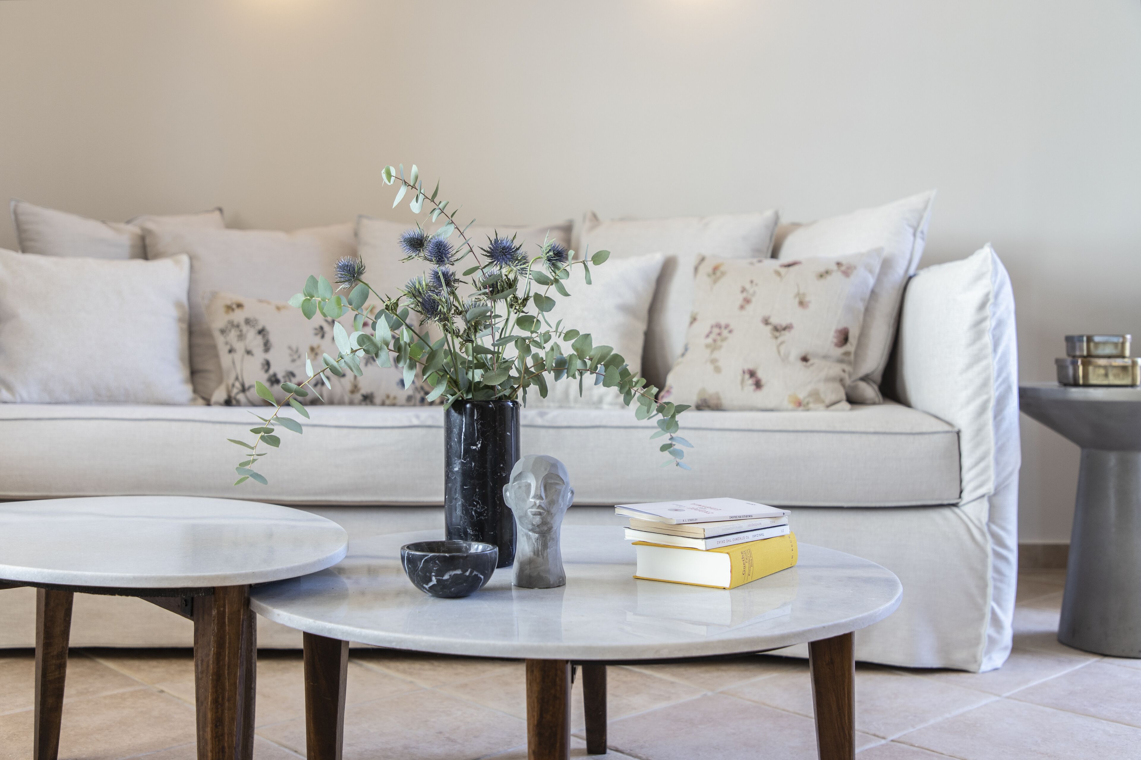 A living room with a sofa, two coffee tables, a vase with flowers, a book, and a sculpture.
