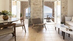A room with a stone wall, a round table with chairs, a sofa, and a view of the sea. - Amani Earthy Living (West Mani)