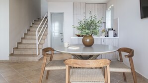 A modern kitchen with a dining area, featuring a round table, two chairs, a vase with flowers, and a staircase leading to another room. - Amani Earthy Living (West Mani)